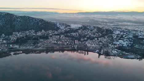 A-drone-shot-of-village-mountain,-warm-weather,-flying-above-a-dreamy-sunrise-reflecting-water-lake,-4K-video,-European-spring-nature,-beautiful-snowy-landscape,-scenic-colorful-clouds