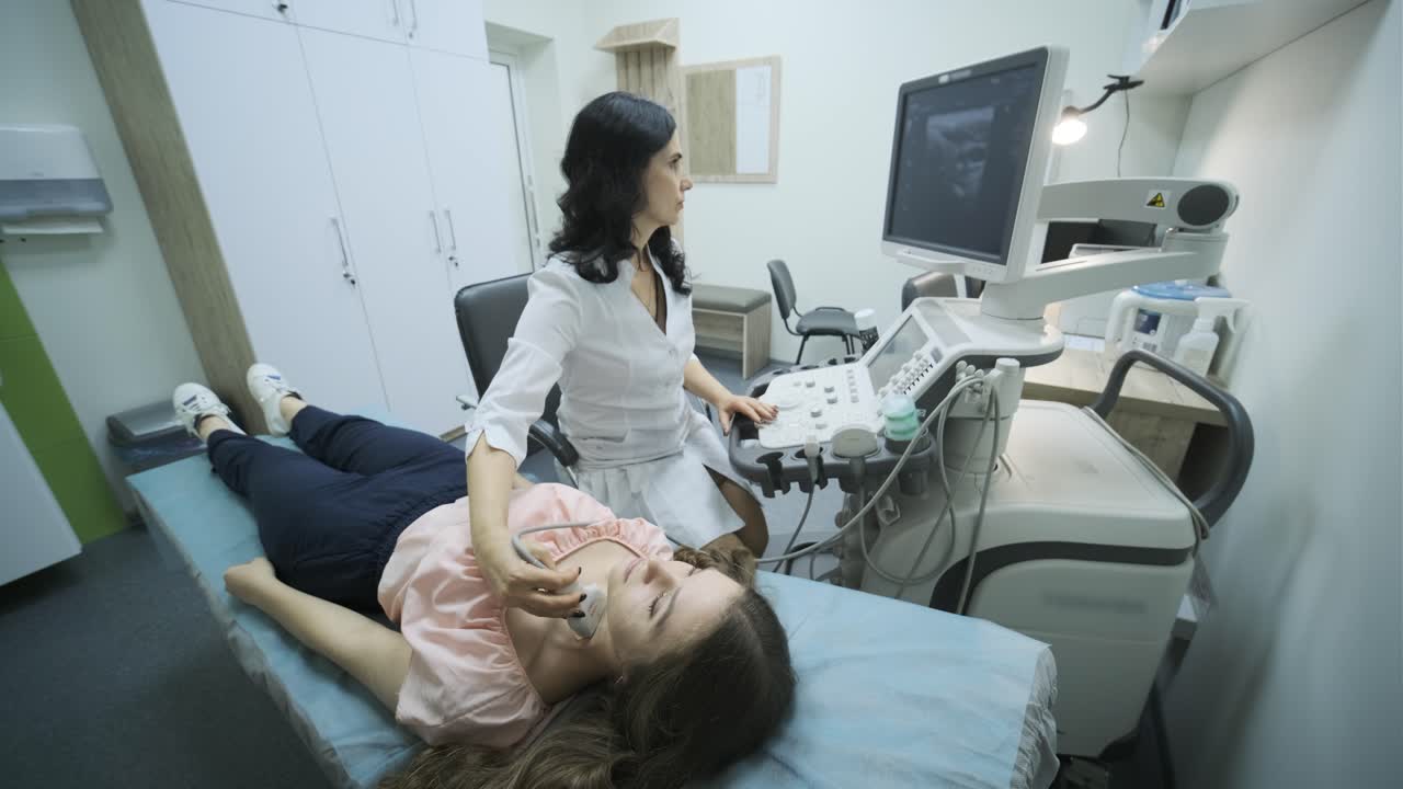 Ultrasound scanning diagnostic of young woman thyroid gland in clinic. Woman doctor runs ultrasound sensor over patient's neck.