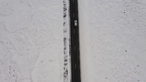 aerial: top down view of one car driving on a snowy road in iceland during winter