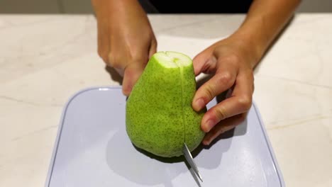 person slicing a pear on a cutting board