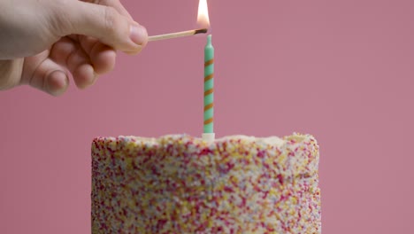 studio shot of revolving birthday cake covered with decorations and single candle being lit