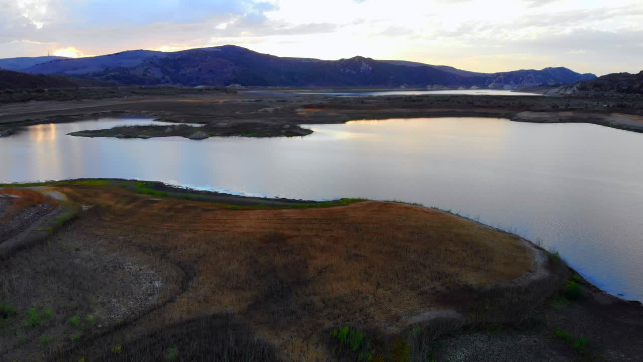 Aerial drone boom down over dried-up Irvine Lake in Southern California at beautiful sunset- lake is almost empty due to drought
