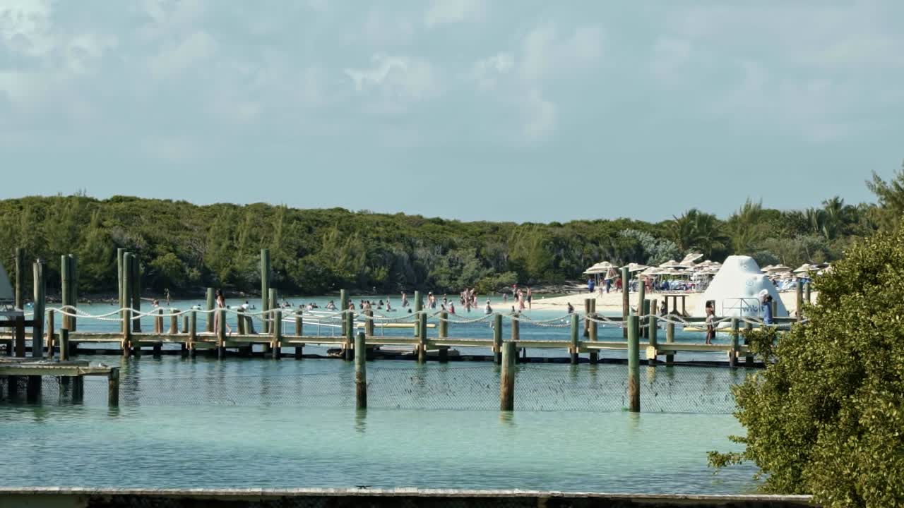 cámara lenta de mano de una hermosa isla del caribe cubierta de pasillos de madera sobre el agua y muchos turistas disfrutando de una hermosa playa tropical de las bahamas en un día nublado de otoño