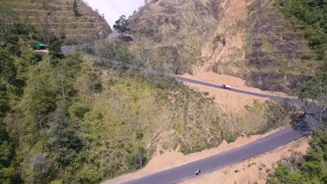 red car driving over a bendy road that leads over a mountain pass