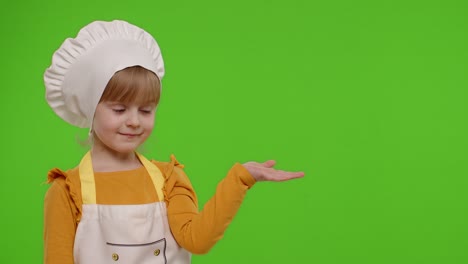 niña vestida como chef cocinero apuntando a la derecha en el espacio en blanco lugar para su logotipo de publicidad