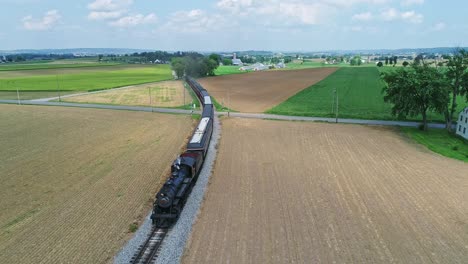 An-Aerial-View-of-an-Approaching-Steam-Passenger-Train,-Blowing-Smoke-and-Steam-on-a-Partially-Sunny-Day