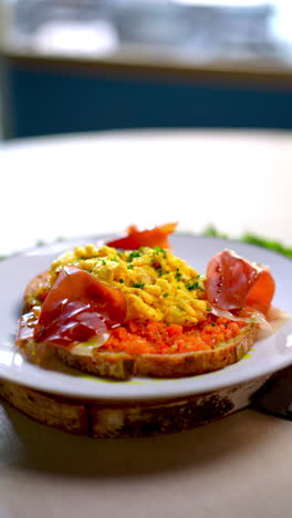eastern european cuisine presents scrambled eggs seasoned with herbs, accompanied by thin slices of ham and a vibrant tomato paste, all served on a slice of toasted bread