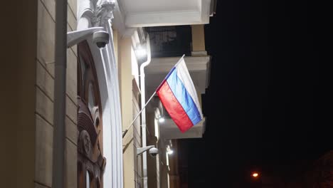 flag of russian federation develops in wind at night on administrative building.