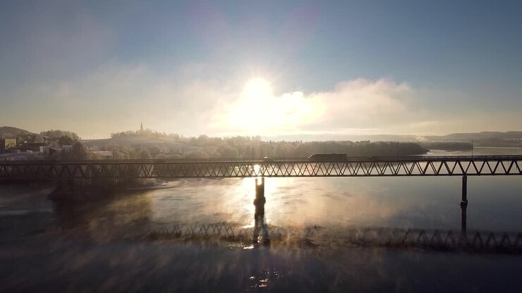 Aerial view of a bridge spanning the Glomma River in Fetsund, Norway, with a stunning sunrise casting reflections on the water