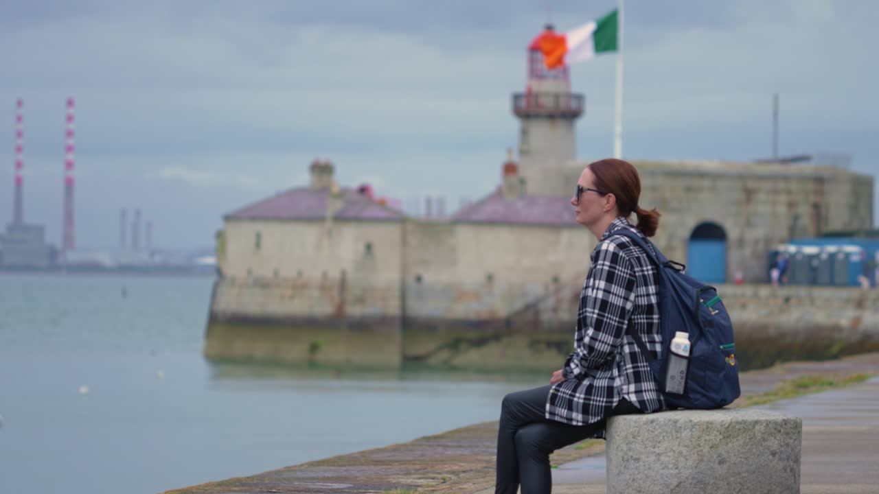 Woman sitting near a lighthouse in Ireland with Irish Flag