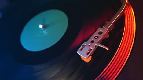 defocus in focus player vinyl records turntable closeup on a background of red and blue lights. the needle slides smoothly on a spinning black vinyl record