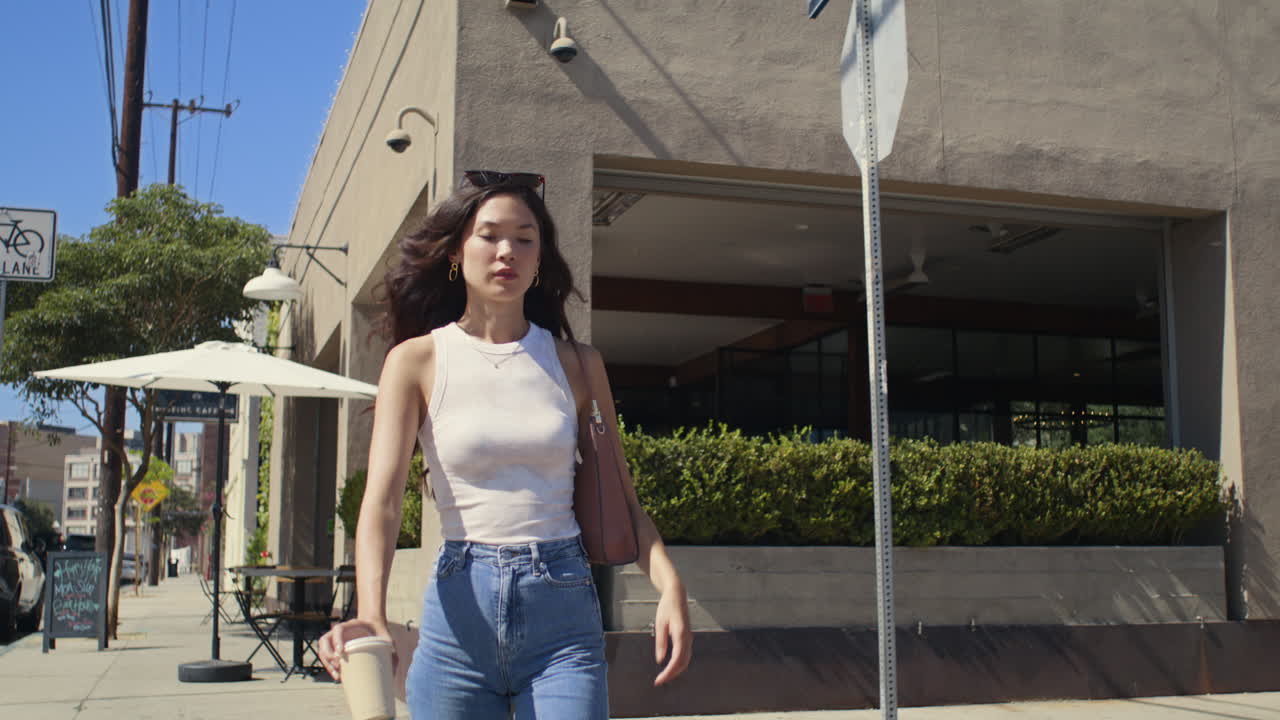 una mujer de moda va a trabajar con una taza de café. una mujer asiática cruza la calle de la ciudad.