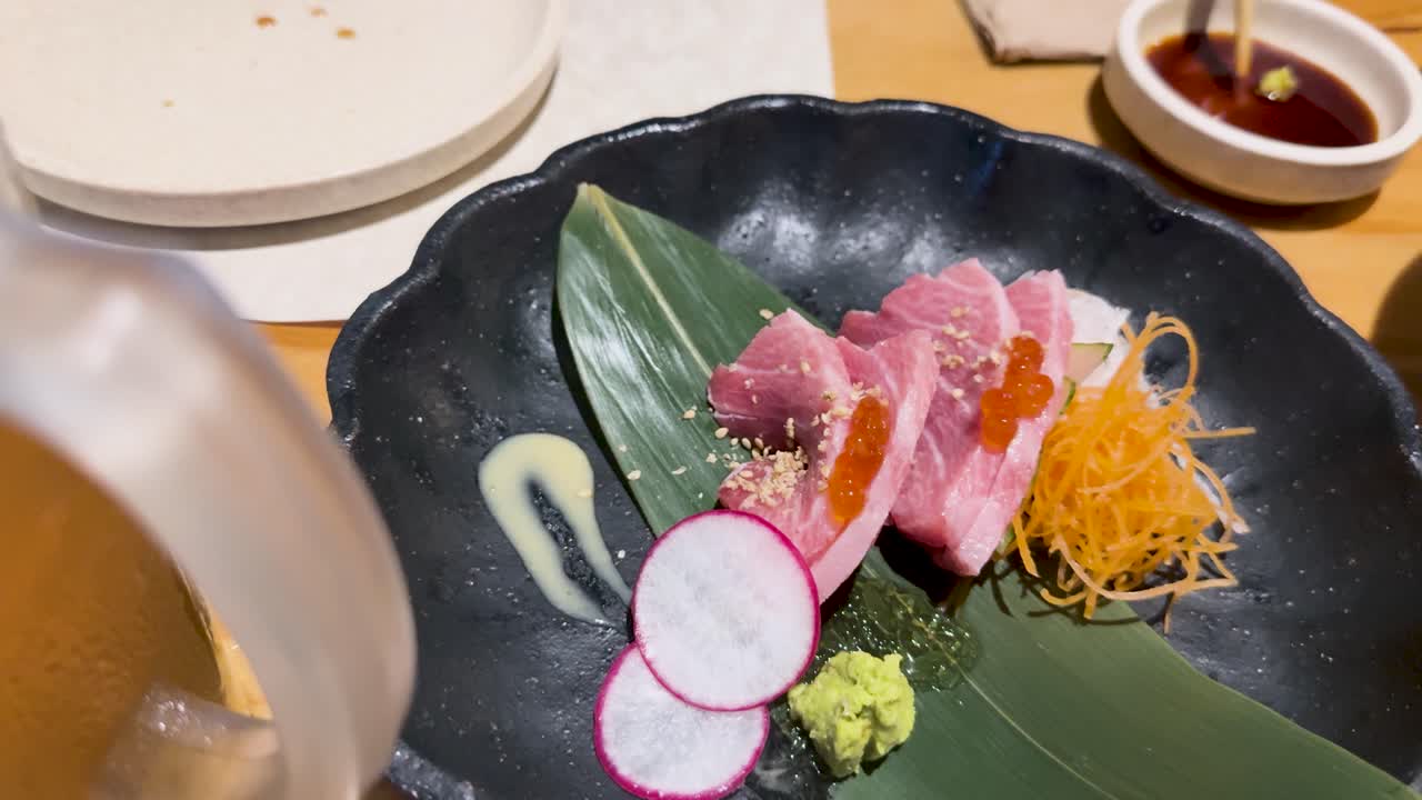 Close-up of toro tuna sashimi on a black plate with wasabi and radish, under bright lighting