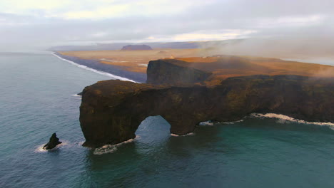 aerial cinematic drone zoom out circling to the left stunning sunrise fog early winter at black sand beach apostles fire and ice ocean next to dyhrolaey lighthouse and cave reynisfjara iceland