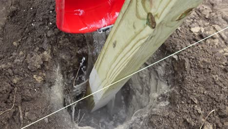 verter agua sobre hormigón en un agujero de poste de cerca y llenarlo con tierra para montar el pilar de la cerca