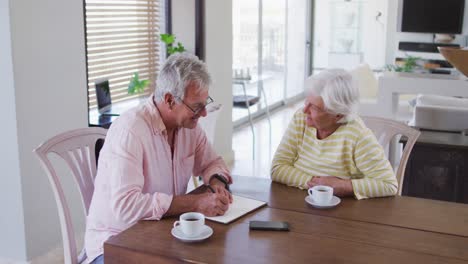 Senior-caucasian-couple-talking-to-each-other-calculating-finances-together-at-home