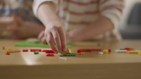 close up of two children playing with plastic construction bricks on table at home 1