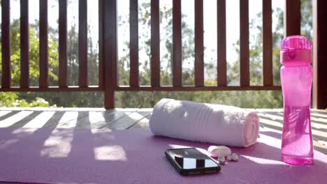 towel, bottle of water, earphones and smartphone on yoga mat at log cabin, slow motion