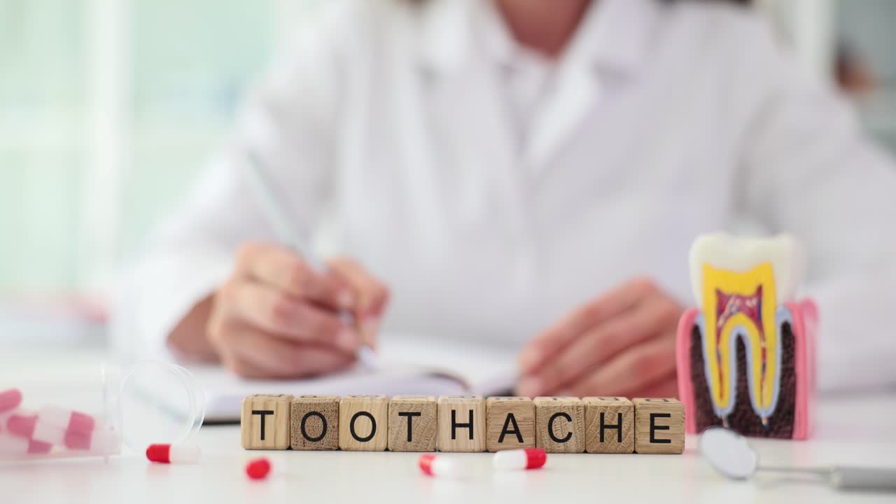 Toothache spelled out with blocks on a desk with dental tools and a doctor in the background, representing dental pain and care