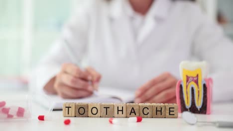 toothache spelled out with blocks on a desk with dental tools and a doctor in the background, representing dental pain and care