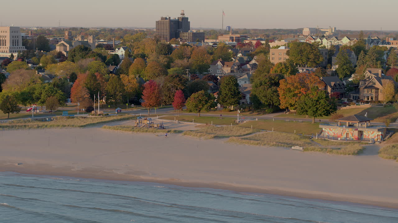 Drone aerial over Sheboygan, Wisconsin neighborhood and buildings along the Lake Michigan shoreline on a clear autumn day with colorful trees and a scenic view