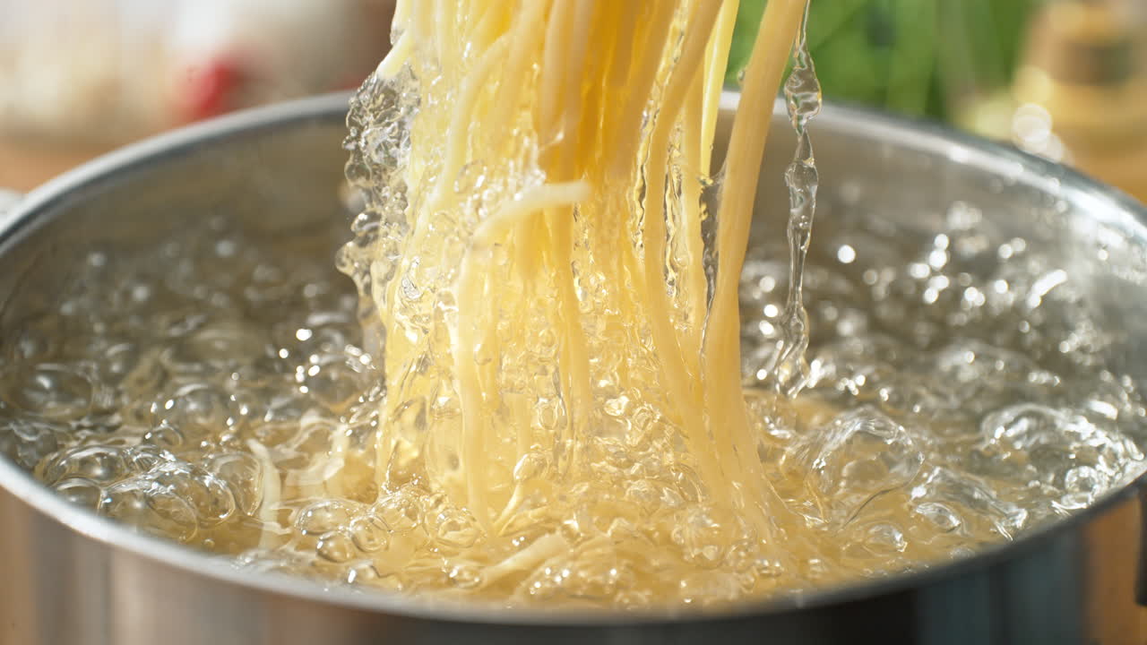 Lifting Cooked Pasta from a Pot of Boiling Water Using Spaghetti Tongs and Splashing Water Droplets in Slow Motion