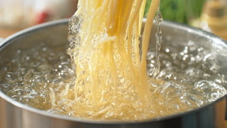 levantar la pasta cocida de una olla de agua hirviendo usando pinzas de espagueti y salpicando gotas de agua en cámara lenta