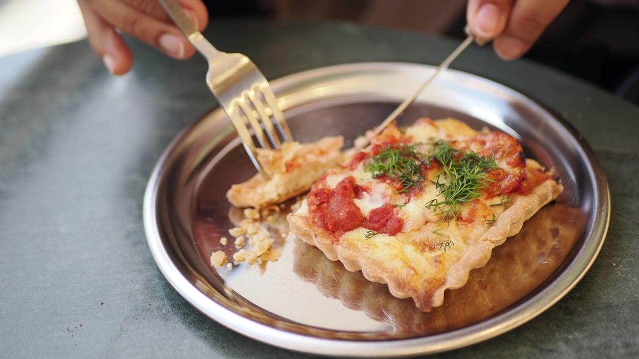 Person schneidet eine köstliche herzhafte Tarte auf einem Metallteller