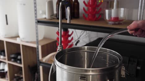 water pouring into and filling up a metal pot in a home beer brewing setup, close up