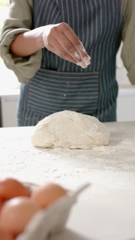 vertical video: sprinkling flour on dough, woman preparing homemade bread in kitchen