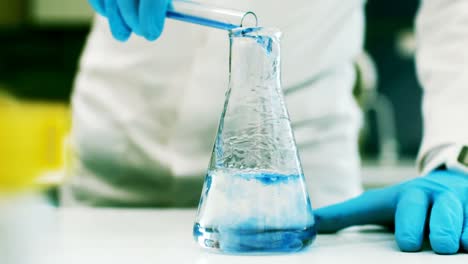 scientist pouring test tube liquid into a erlenmeyer flask