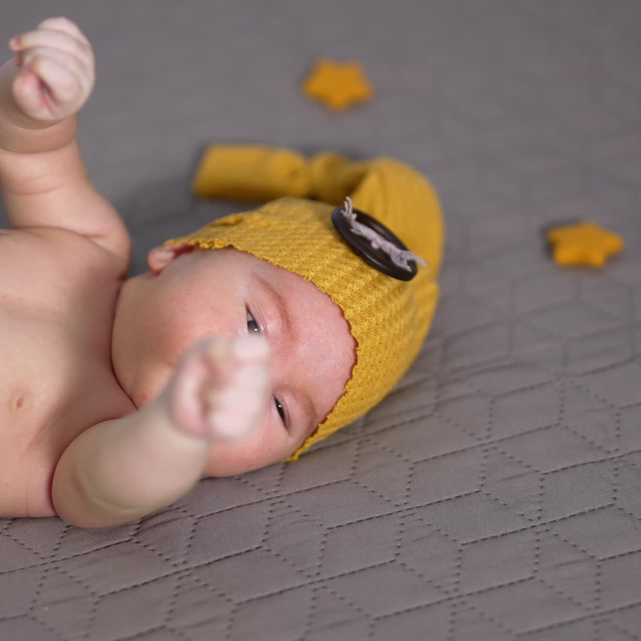 Sweet baby lying on the bed and moving his little fists randomly. Newborn wearing yellow costume and surrounded by toy stars close up