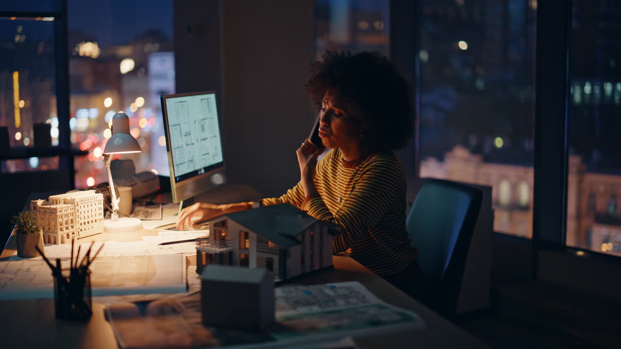 Manager sopraffatto che parla al cellulare in un'agenzia di architettura in un ambiente di lavoro buio