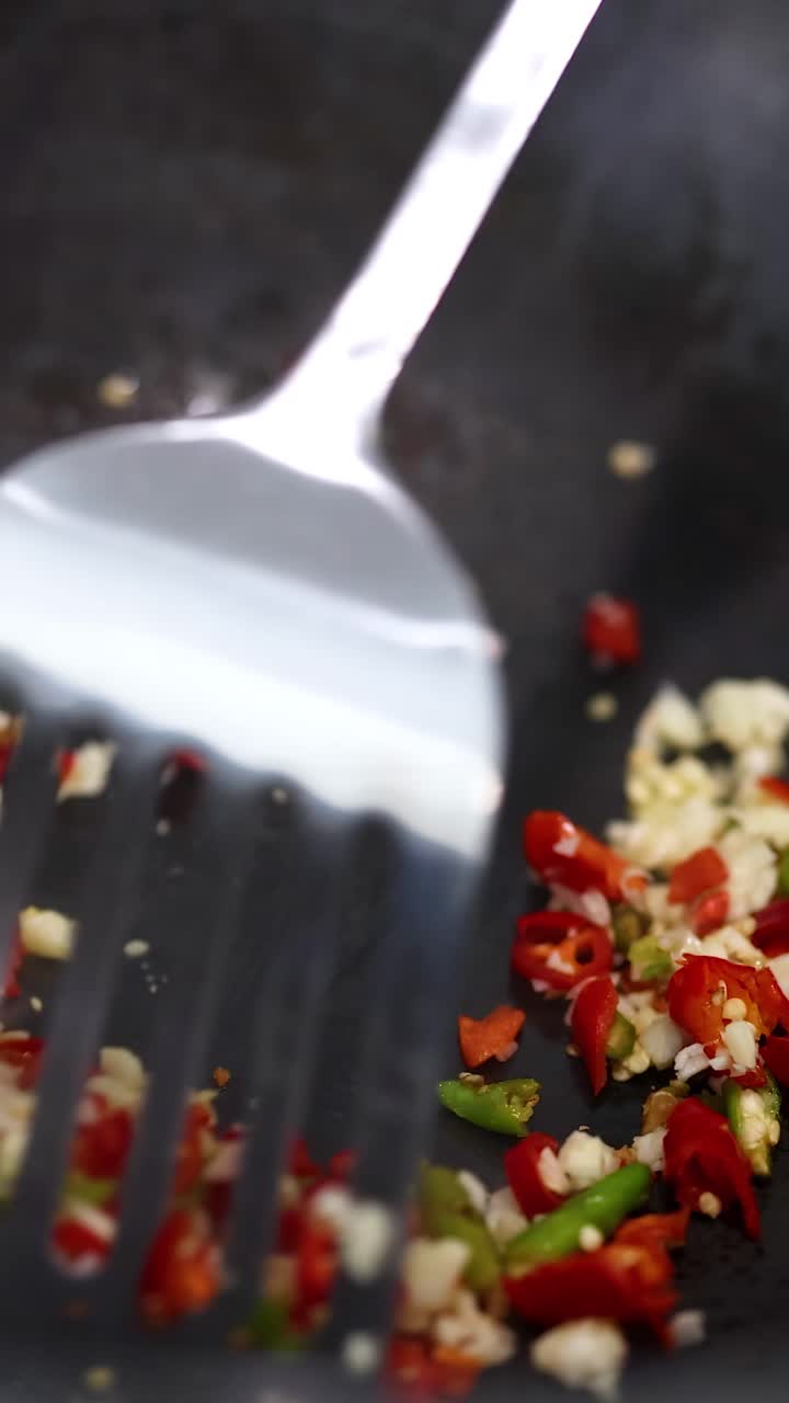 Close-up of vibrant chilli and garlic being stir-fried in a pan with a spatula