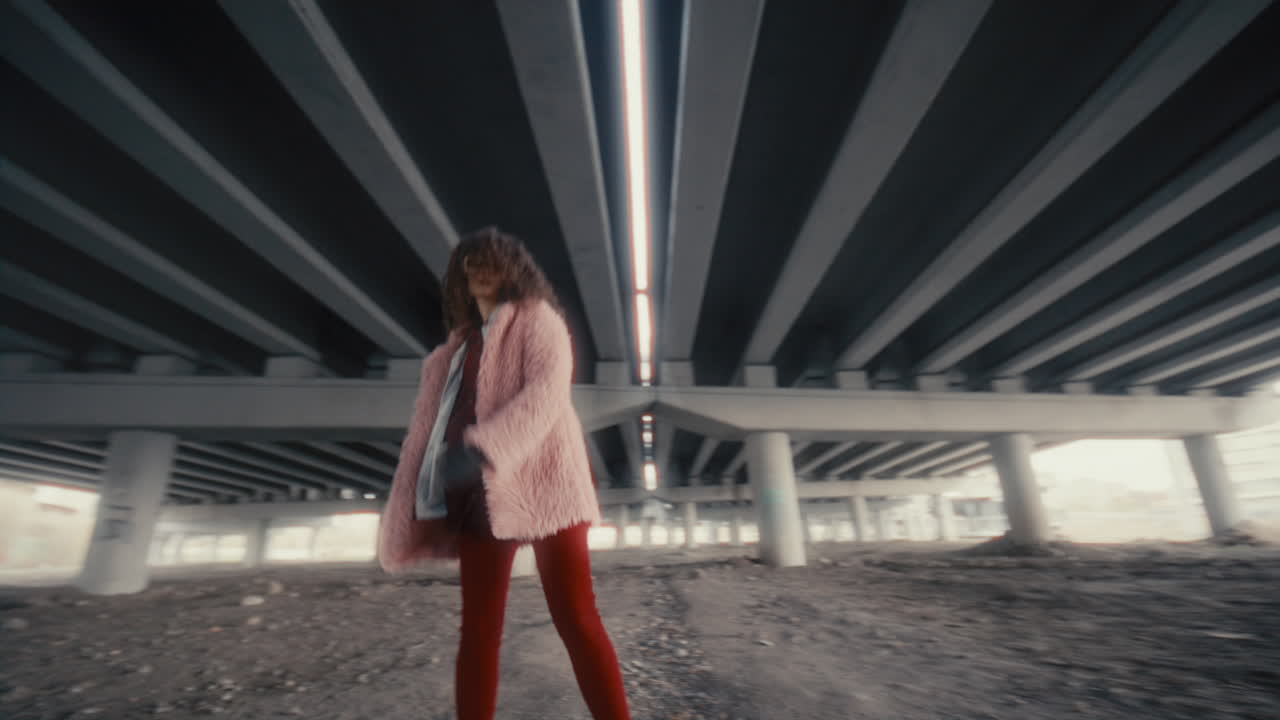 Relaxed Girl in Stylish Outfit Dancing for Camera under Concrete Overpass