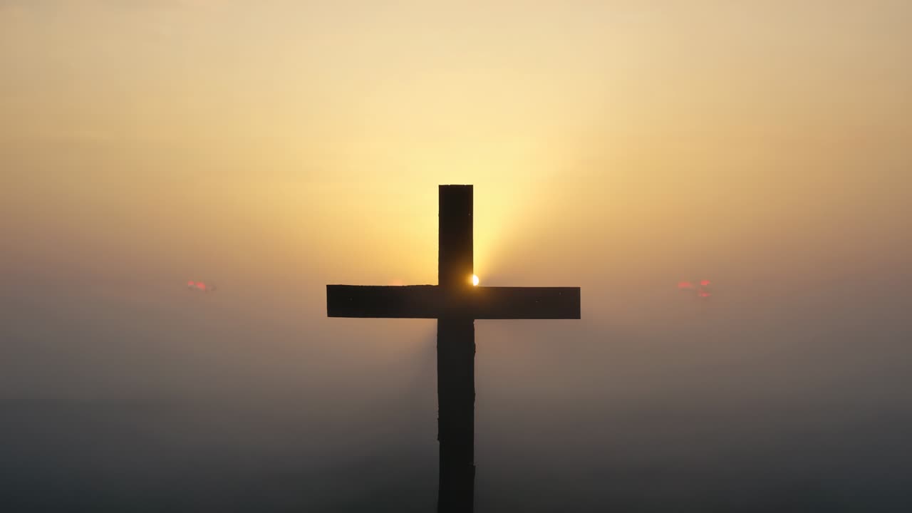 Emerging dawn light illuminating wooden cross on misty hill, revealing sun rising behind beam