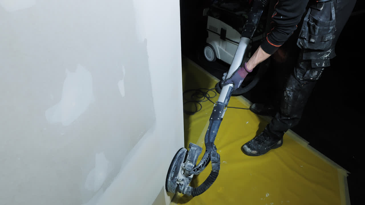 Dust-free sanding process as worker smooths plaster wall on yellow floor cover
