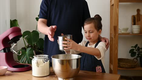 father and daughter sifting flour into mixing bowl