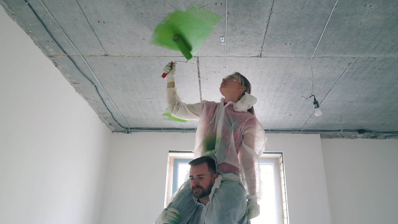 hombre sostiene mujer pintando el techo con color verde en la habitación