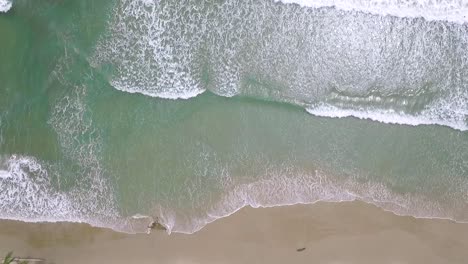 from the top view of a light blue sea breaking in a sandy beach