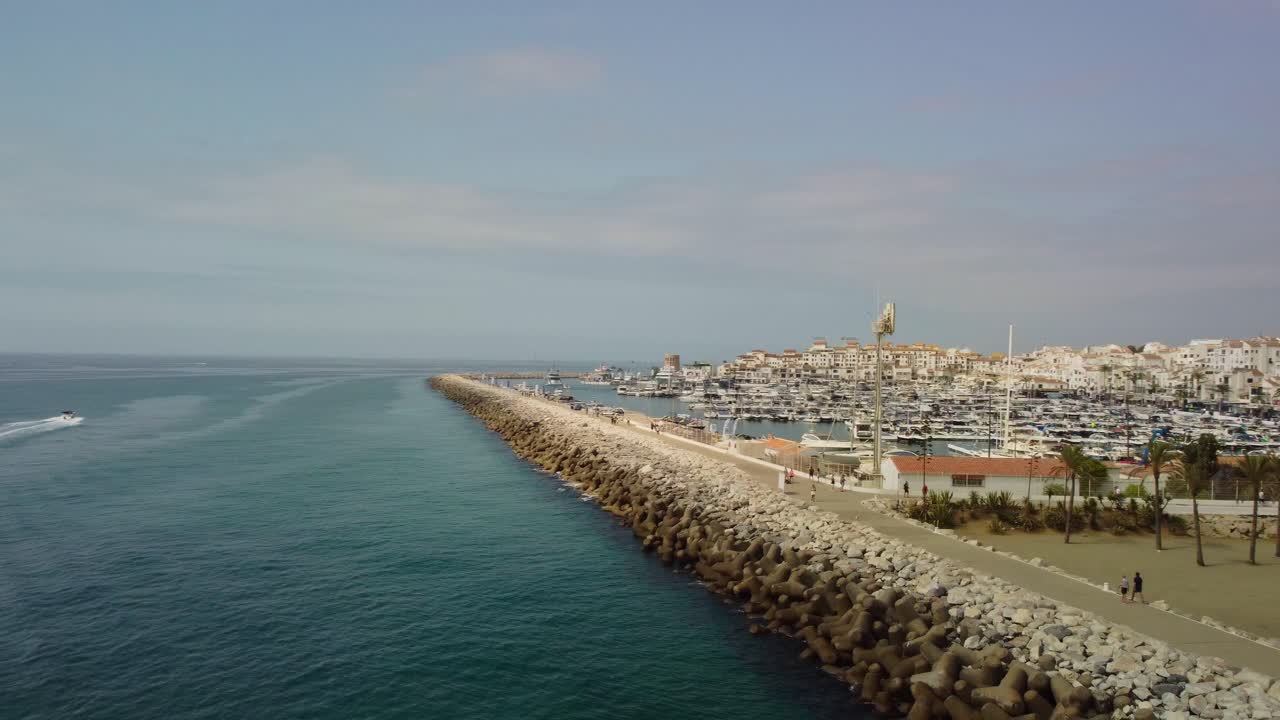 Marina di Puerto Banús a Marbella con imbarcazioni da diporto e un motoscafo in movimento, cielo sereno, vista aerea
