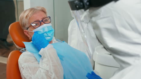 mujer anciana con traje de protección tocando la cara con dolor de dientes