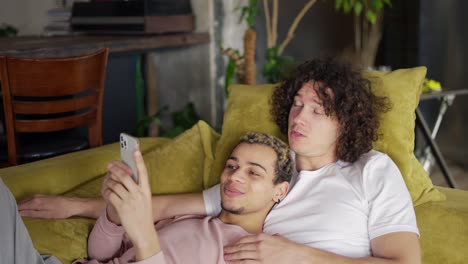 male romantic gay couple relaxing on the couch, watching the smartphone screen