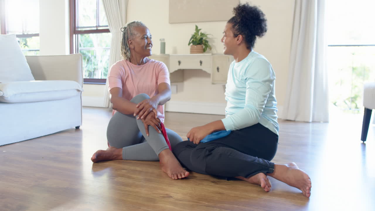 Senior woman and caregiver exercising with resistance bands at home, sharing smile
