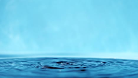 slow motion 4k video of a water surface with falling drops on a blue background. splashing water. studio shooting.