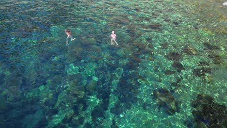 two tourists swimming in the transparent waters of ibiza, spain. unique aerial view flight drone shot footage from above
