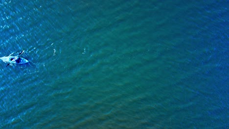 Recreational-Kayaking-on-a-lake-during-a-sunset-as-person-paddles-into-the-sunset-reflective-blue-green-waters-with-an-aerial-drone-Birds-eye-view-of-steady-strokes-as-the-is-wearing-a-life-jacket