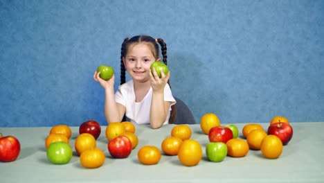 Portrait of a cute little girl with fruits indoors. Ripe fruit on the table. Beautiful smiling child playing with fresh apples on the table.