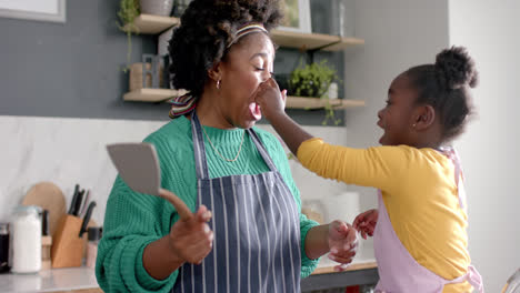 Happy-african-american-mother-and-daughter-fooling-around-in-kitchen,-slow-motion