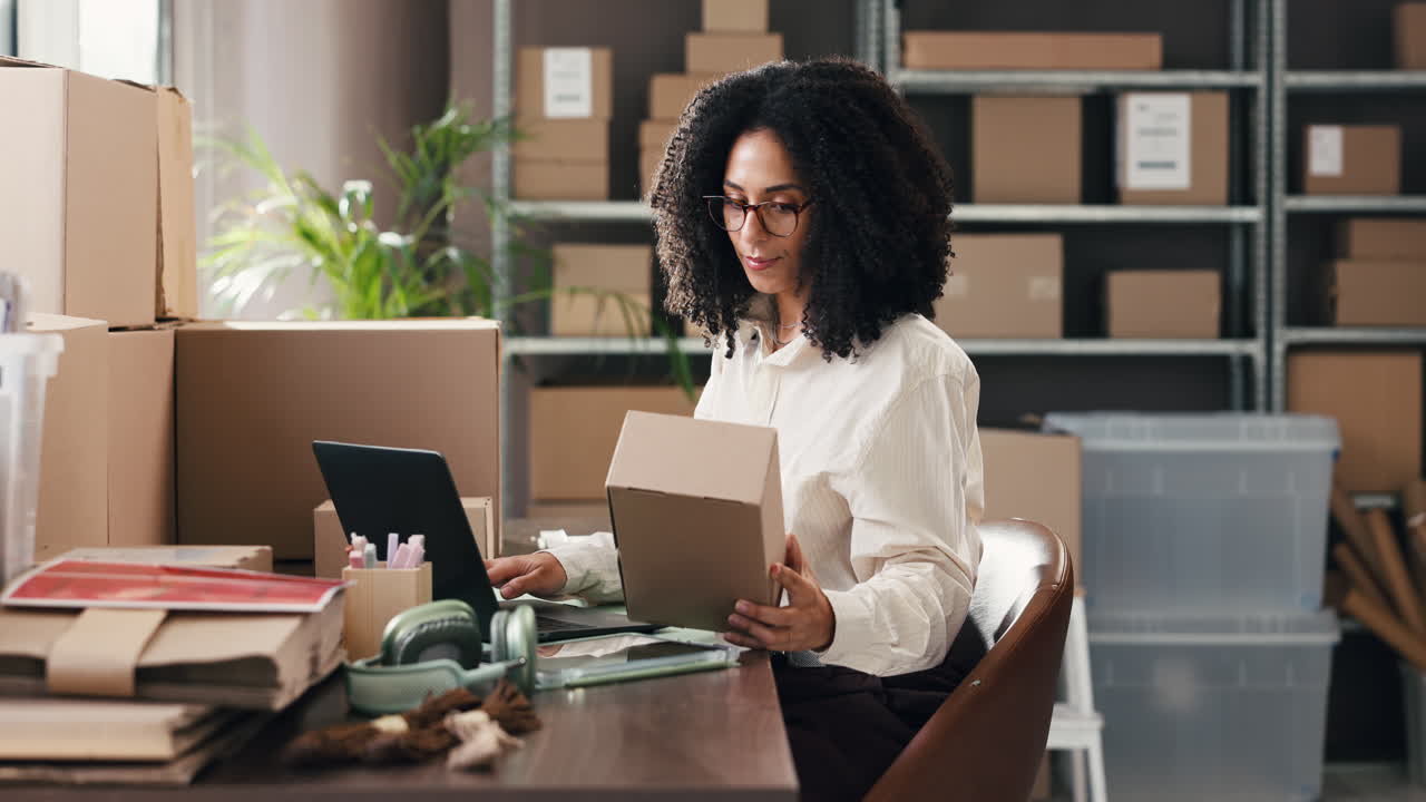 Woman Working on Laptop and Holding Box in E-commerce Office